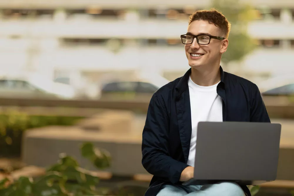 Jeune homme souriant profite de son style de vie en travaillant sur son ordinateur portable