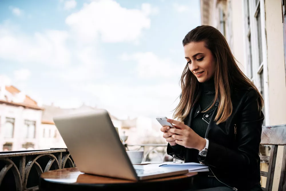 Jeune femme au café, utilisant son téléphone et son ordinateur portable