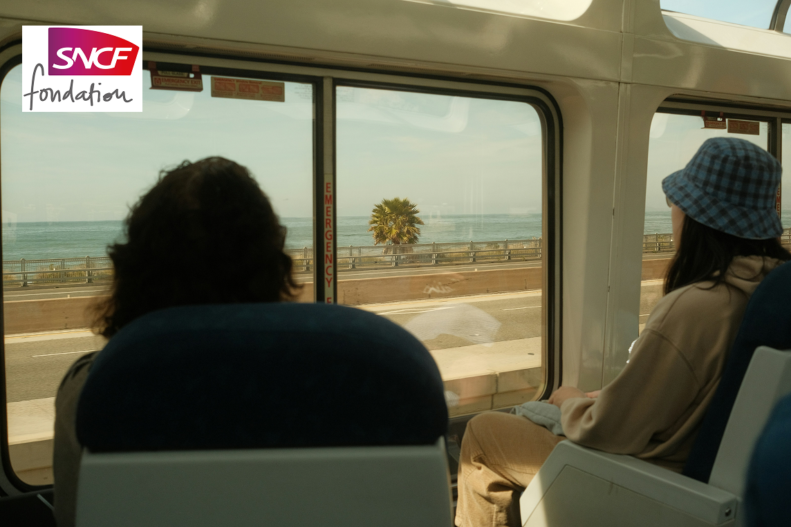 A man and a woman inside a train looking outside, at the sea