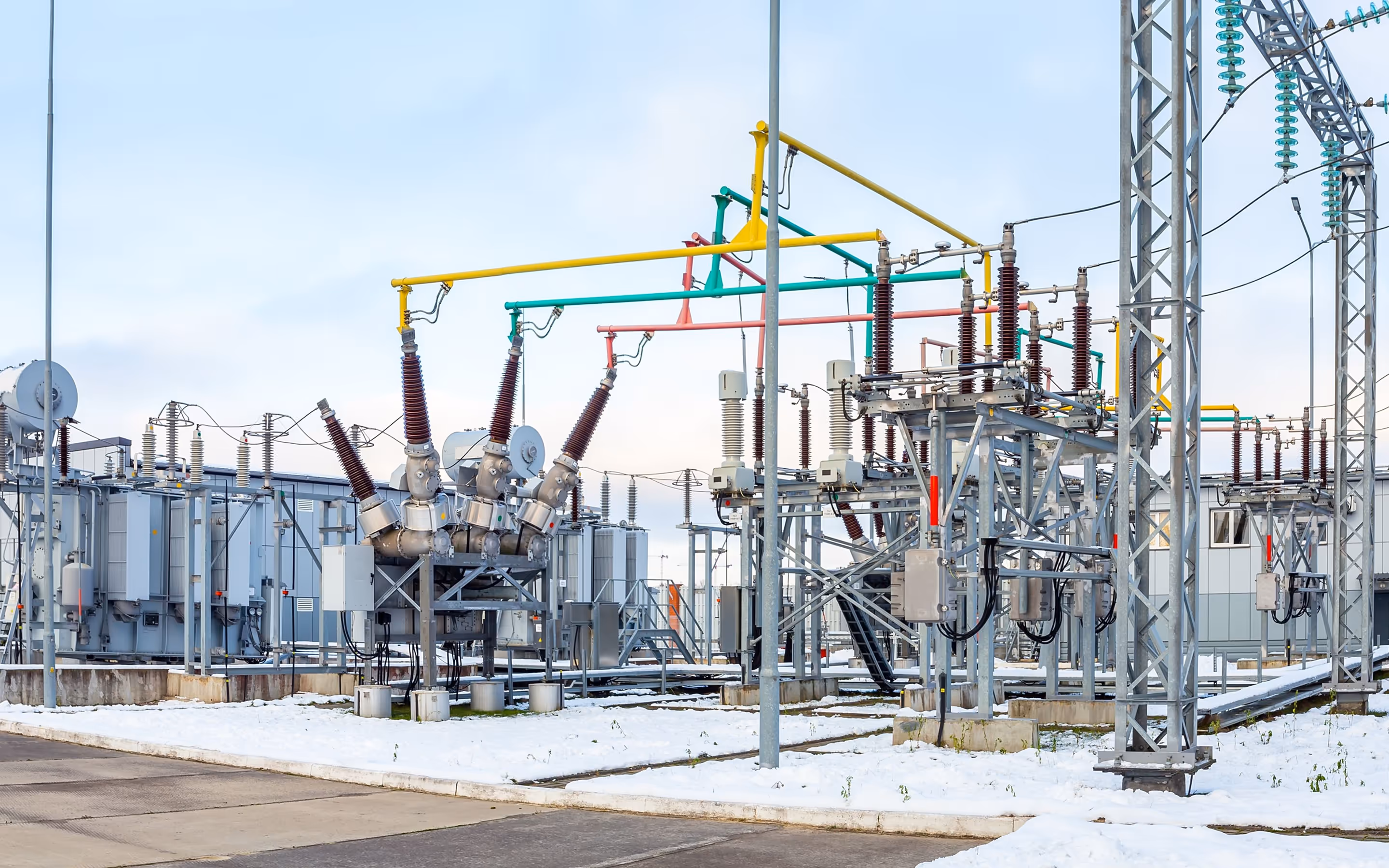 Outdoor electrical substation with transformers and colorful overhead power lines on a snowy ground under a clear sky.