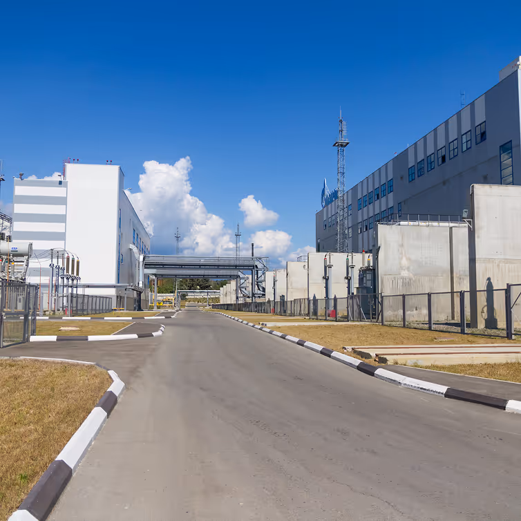 Empty paved road between modern industrial buildings under a clear blue sky with white clouds.