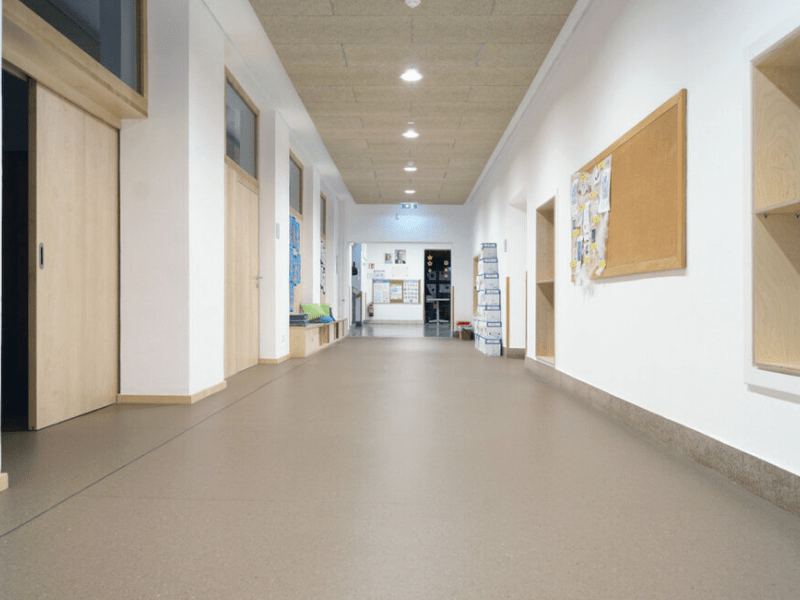 Modernes Badezimmer mit hellen Steinfliesen, weißem Waschbecken, großem Spiegel, Holzablage und einer weißen Polsterbank mit dunklem Kissen.