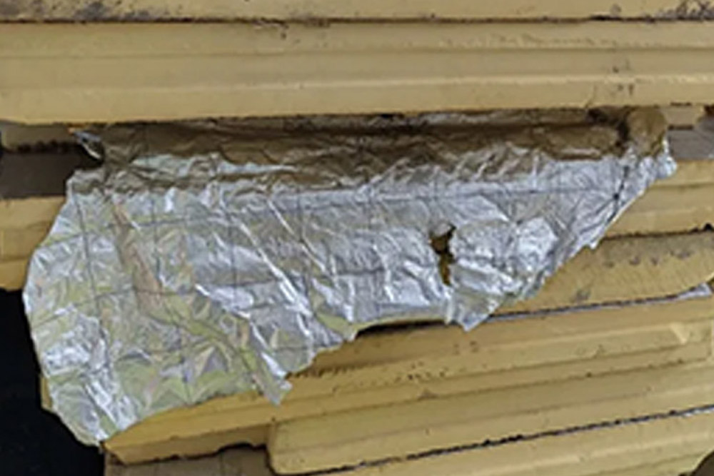 Stos żółtych płyt termoizolacyjnych PIR/PUR z rozerwaną, pomiętą i odchodzącą folią aluminiową (pazłotko / sreberko). Widoczne mechaniczne zniszczenie warstwy ochronnej – klasyczny przykład jednej z głównych wad popularnych materiałów termoizolacyjnych: łatwego rozwarstwiania i uszkodzeń folii aluminiowej podczas magazynowania, transportu, montażu lub użytkowania i mycia myjką ciśnieniową.