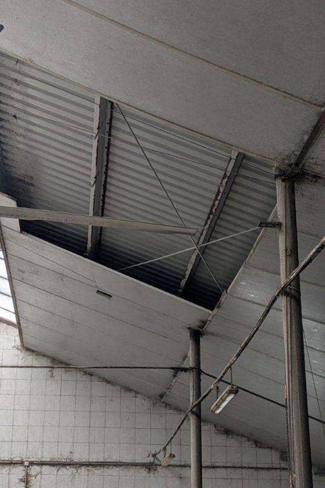 Opadająca podsufitka PIR w budynku inwentarskim – odsłonięta blacha trapezowa po utracie oparcia w profilach maskujących.