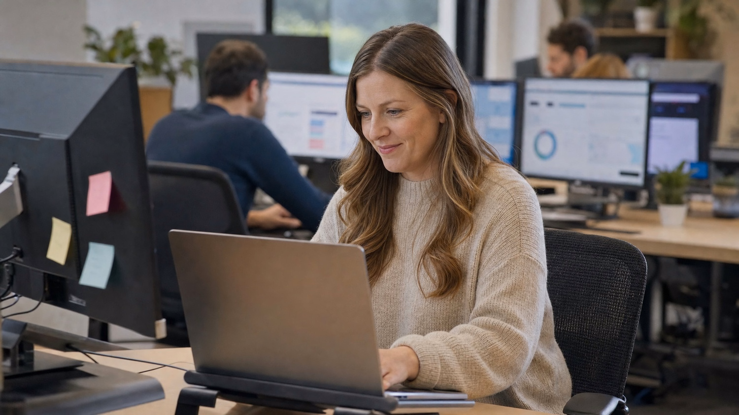Woman at desk working on laptop with sticky notes 61 chars