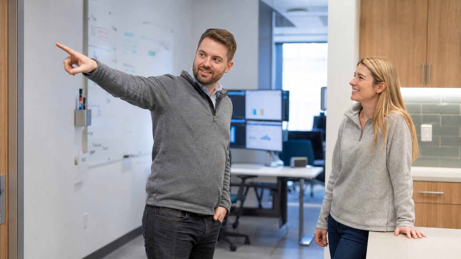 Colleagues discuss whiteboard near kitchen counter
