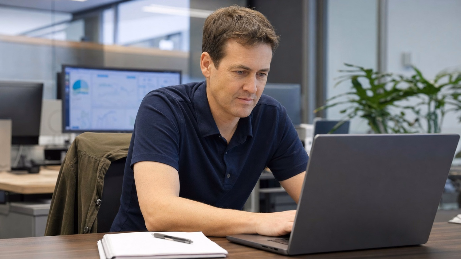 IT professional examines laptop screen, notebook nearby