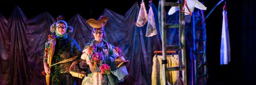 Two performers smiling and standing in floral decorated costumes.