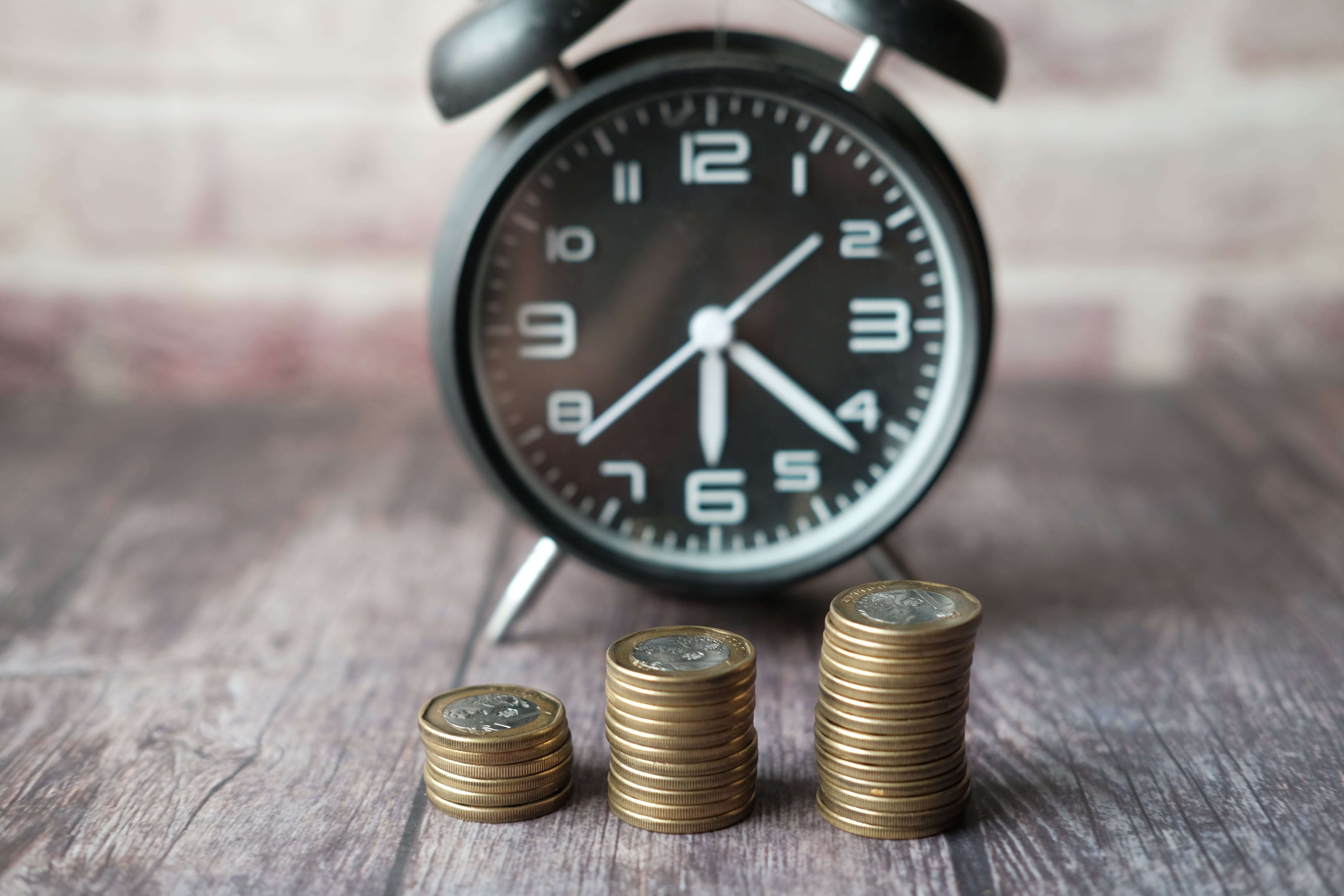 A clock in the background symbolizing timely payments, with three stacks of coins in the foreground. Each stack represents increasing financial stability over time, emphasizing our commitment to providing a fixed income every month. The image reflects our dedication to prioritizing agreements for your financial security, allowing you to focus on what truly matters.