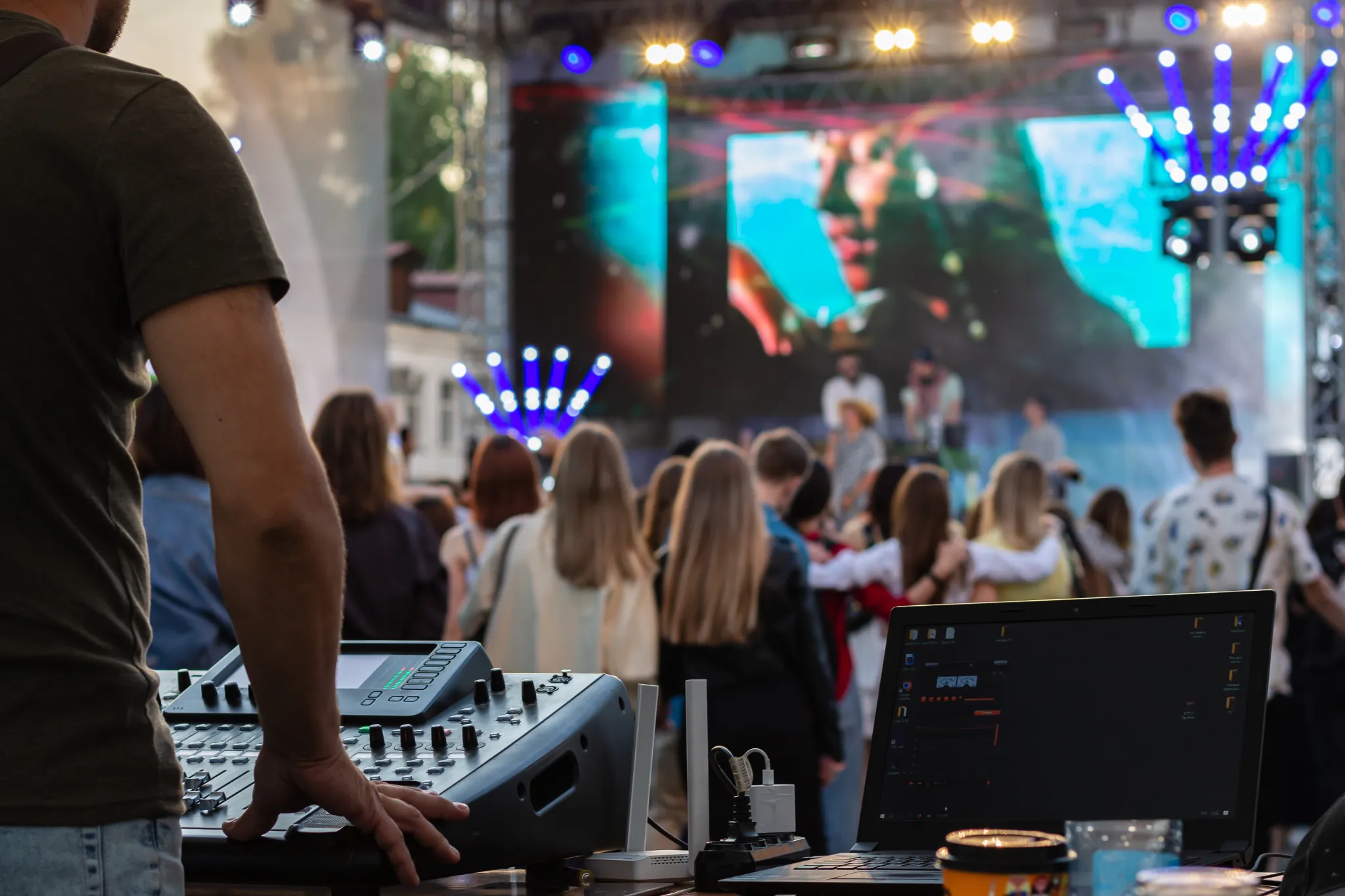 Event management terms you should know about illustrated by a live outdoor concert, showing a sound engineer managing audio equipment and a laptop while a crowd enjoys a performance on stage with vibrant lighting.