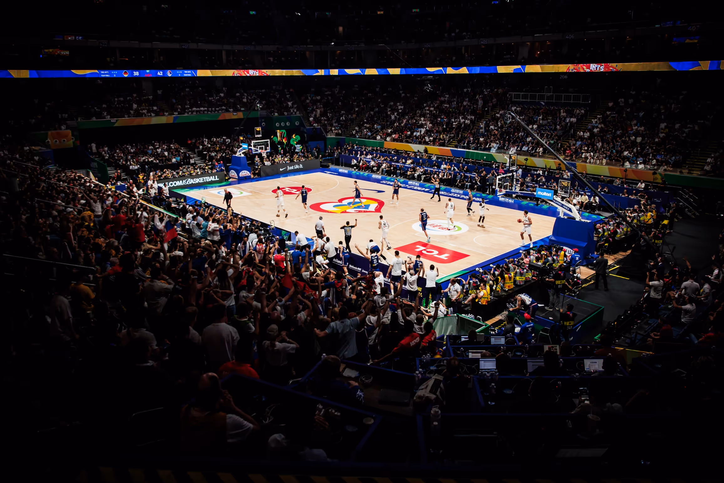 Indoor basketball arena during a FIBA Basketball World Cup 2023 game, with players on court and fans in the stands at the multi-host event in the Philippines, Japan and Indonesia.