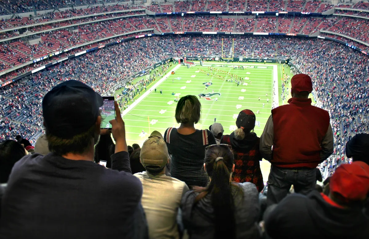Crowd of sports fans watching an American football game inside a packed stadium.