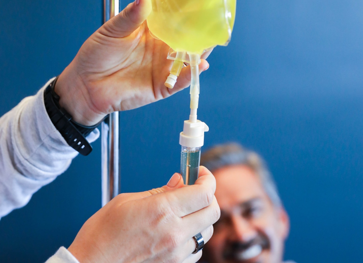 Hands of nurse putting ingredients into NAD IV Therapy bag. Customer smiling in background.