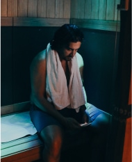 Man sitting in sauna with towel around shoulders.