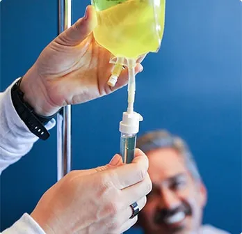 Hands adjusting NAD Therapy drip with smiling man in background.