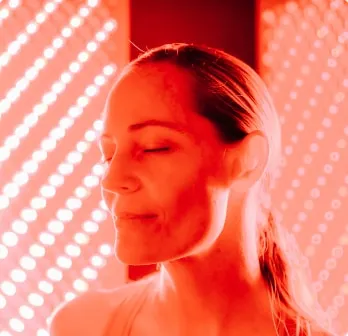 Woman with eyes closed receiving benefits of Red Light Therapy.