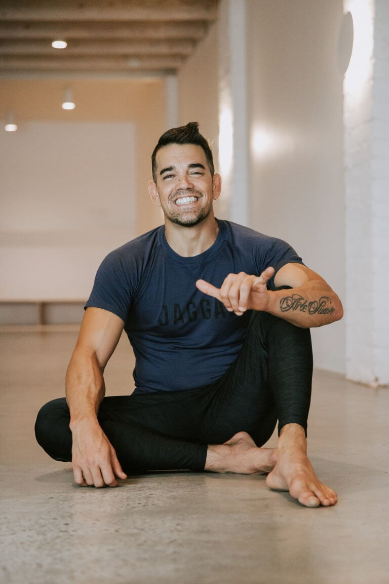 Dustin brown sits on the ground smiling in his warrior one yoga studio
