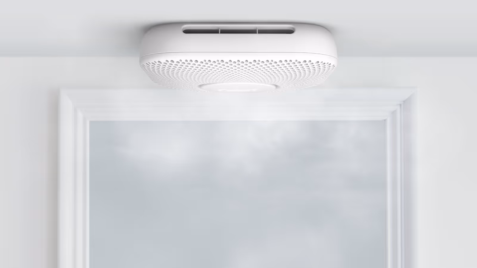 A white Google Nest Protect smoke and carbon monoxide detector mounted on a ceiling. Wisps of smoke rise toward the device, illustrating its sensing function.