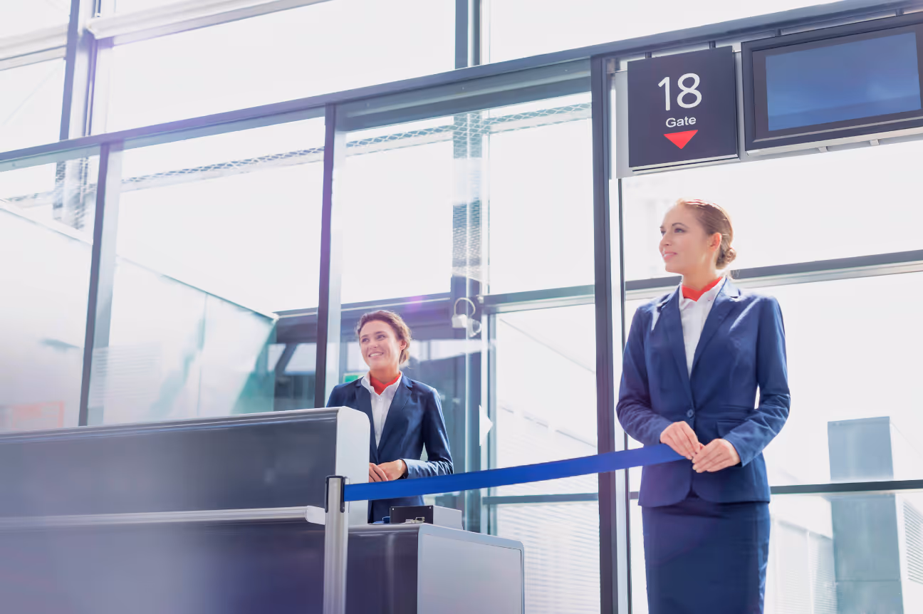 Two smiling airline gate attendants in uniform standing at a boarding gate counter, ready to assist passengers.
