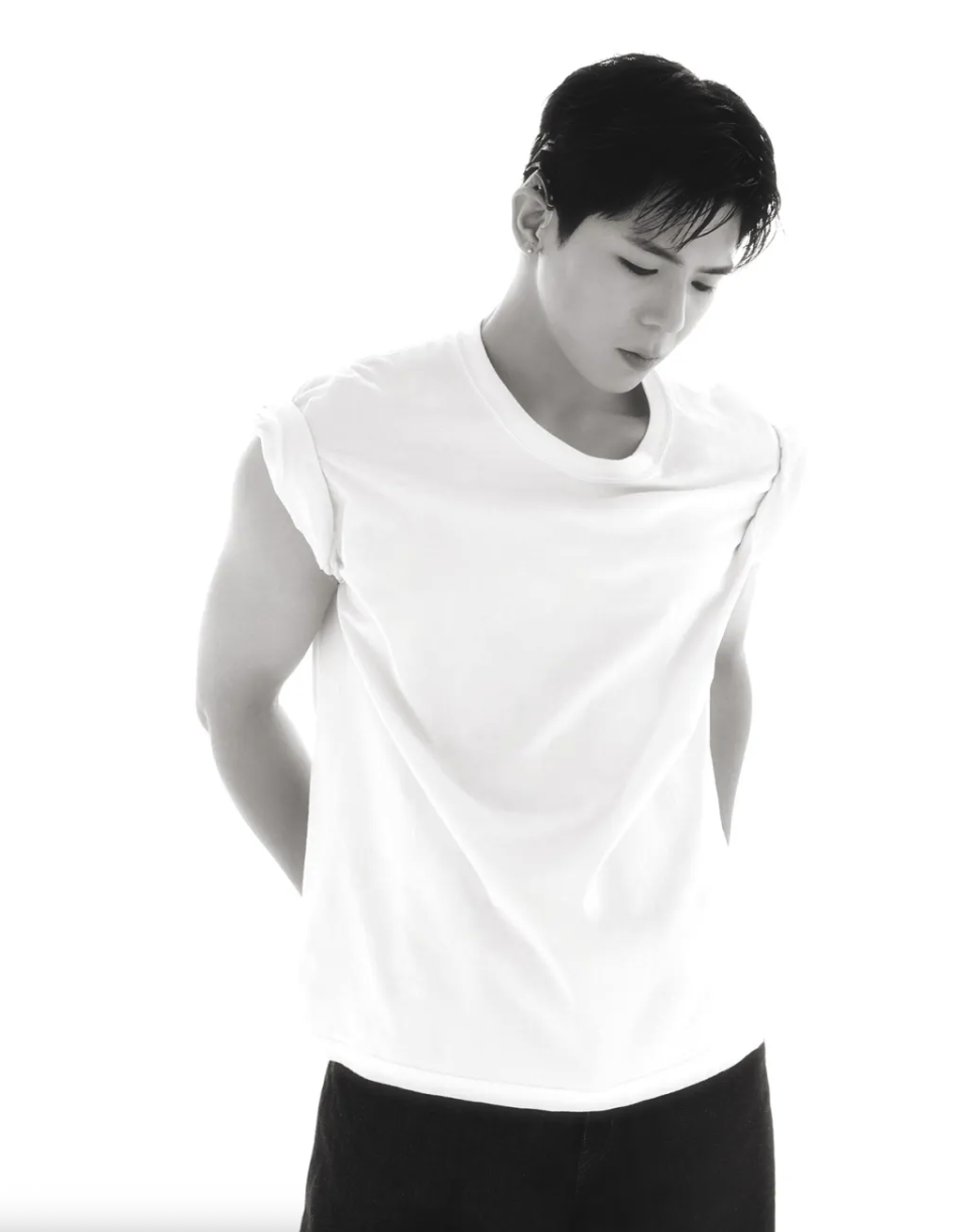A black-and-white portrait of a Big Ocean member in a black jacket layered over a white shirt, looking downward with hands in pockets.