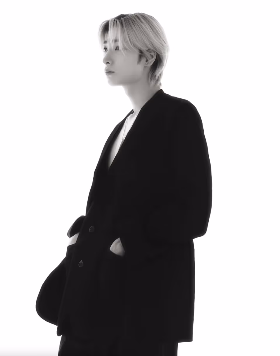A black-and-white portrait of a Big Ocean member with light hair, wearing a black blazer over a white shirt, gazing to the side with hands in pockets.