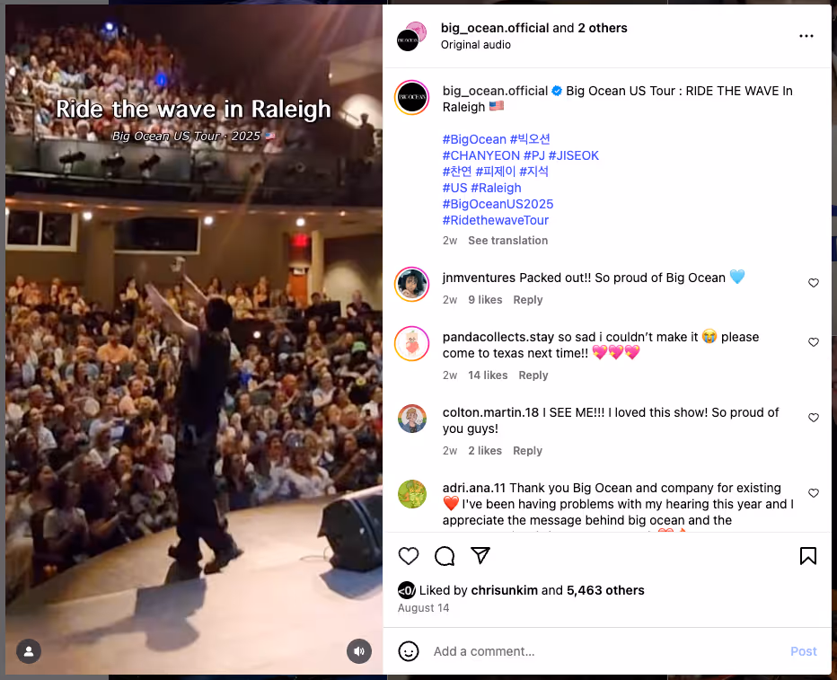 A member of Big Ocean performs on stage during their U.S. tour stop in Raleigh, raising his arms toward a packed audience signing and cheering from the seats.
