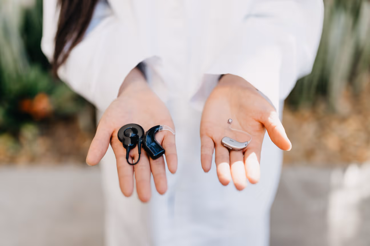 Close-up of a healthcare professional holding two different types of hearing aids and cochlear implant processors in their hands.