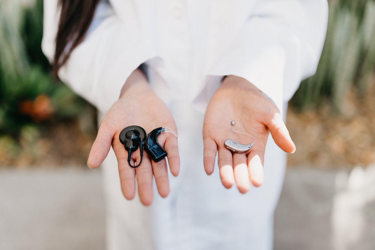 Close-up of a healthcare professional holding two different types of hearing aids and cochlear implant processors in their hands.