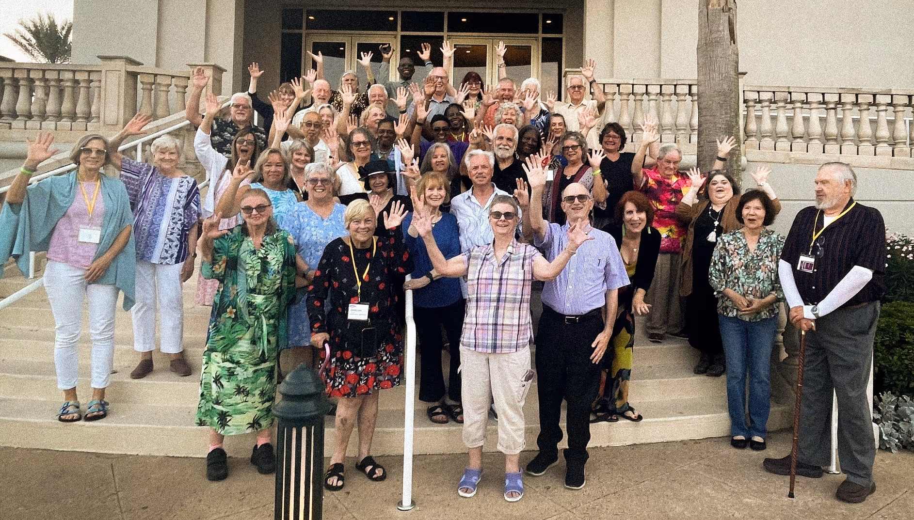 A large group of SayWhatClub members gathered on the steps outside a building during the 2023 Galveston convention, smiling and waving at the camera.
