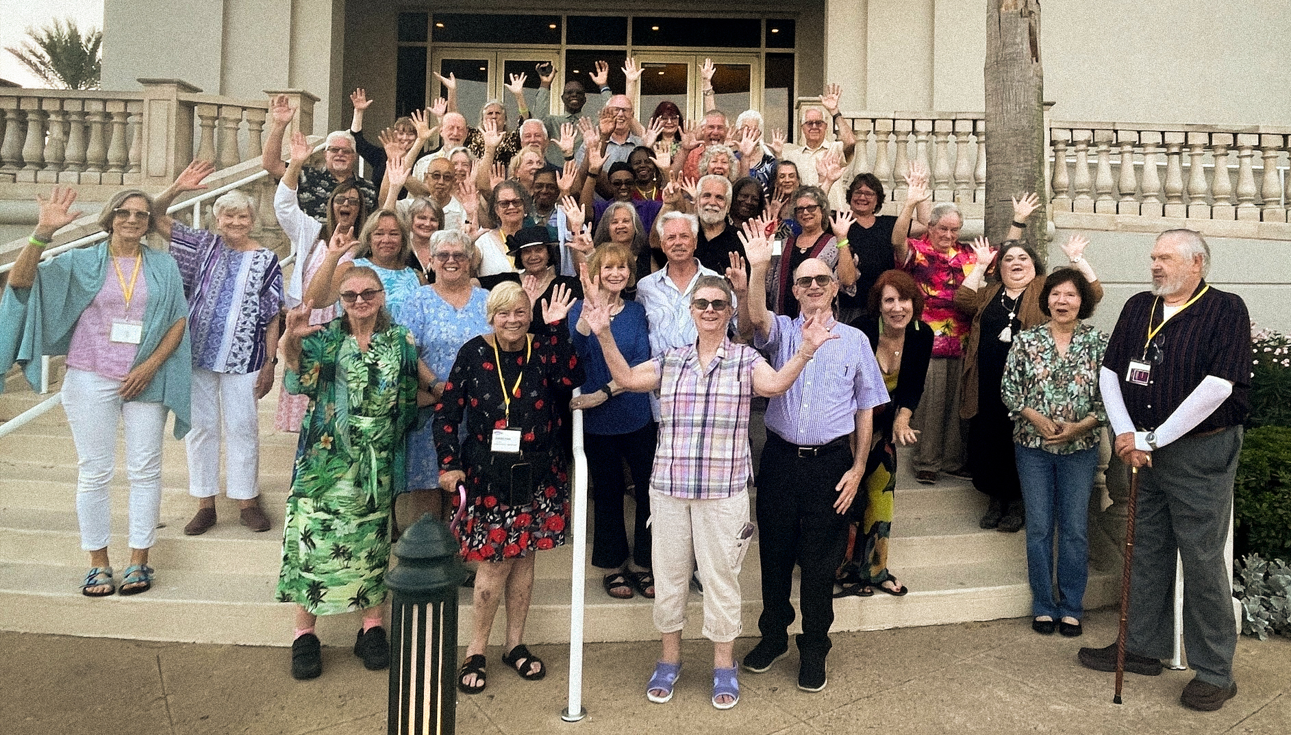 A large group of SayWhatClub members gathered on the steps outside a building during the 2023 Galveston convention, smiling and waving at the camera.