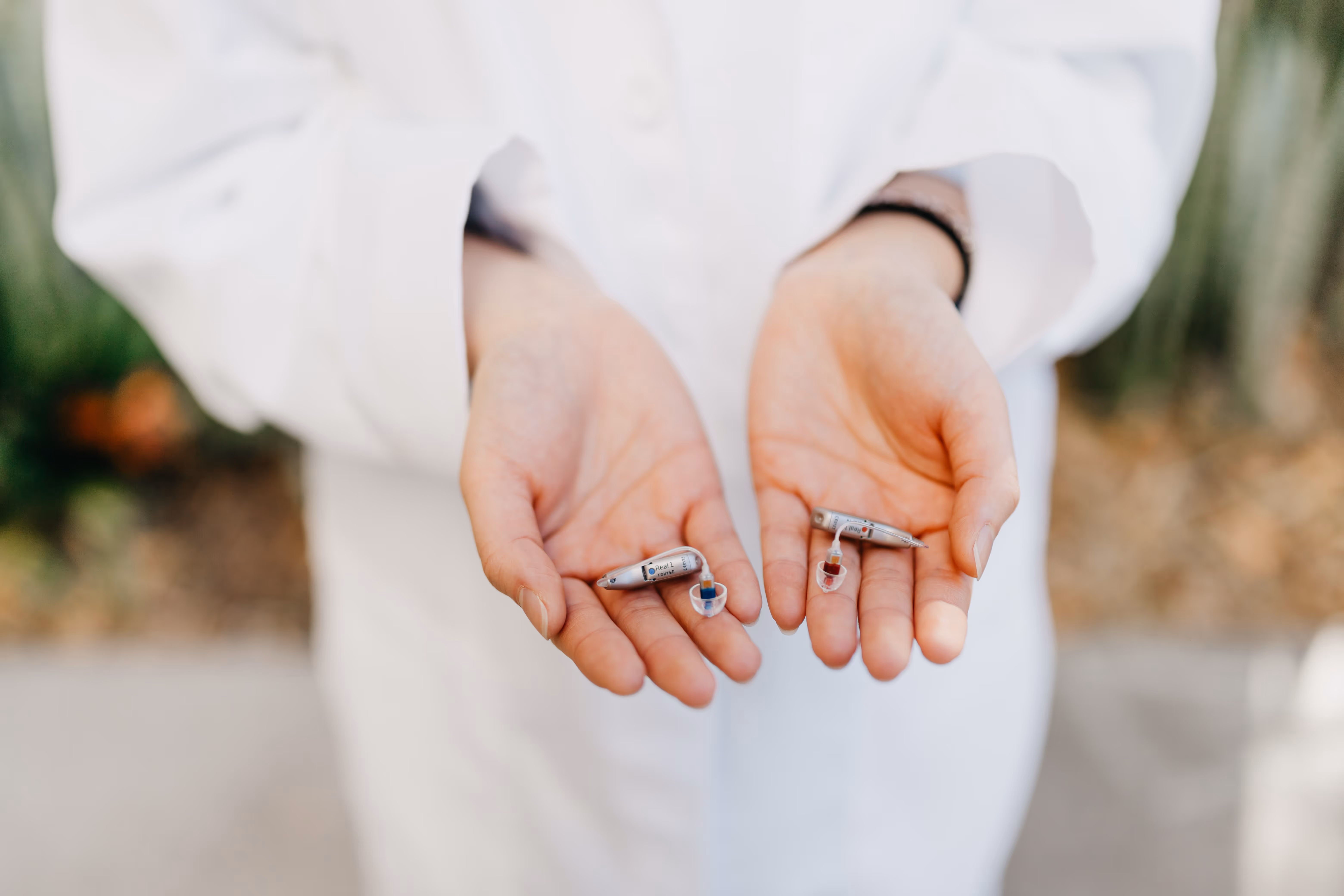 Close-up of an audiologist in a white coat holding two discreet in-the-ear hearing aids. The small, modern devices illustrate today’s advanced hearing technology designed to improve communication for people with mild to moderate hearing loss.
