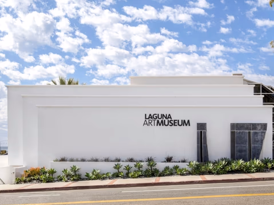 The exterior of the Laguna Art Museum on a sunny day, featuring its modern white façade and bold black signage against a bright blue sky.