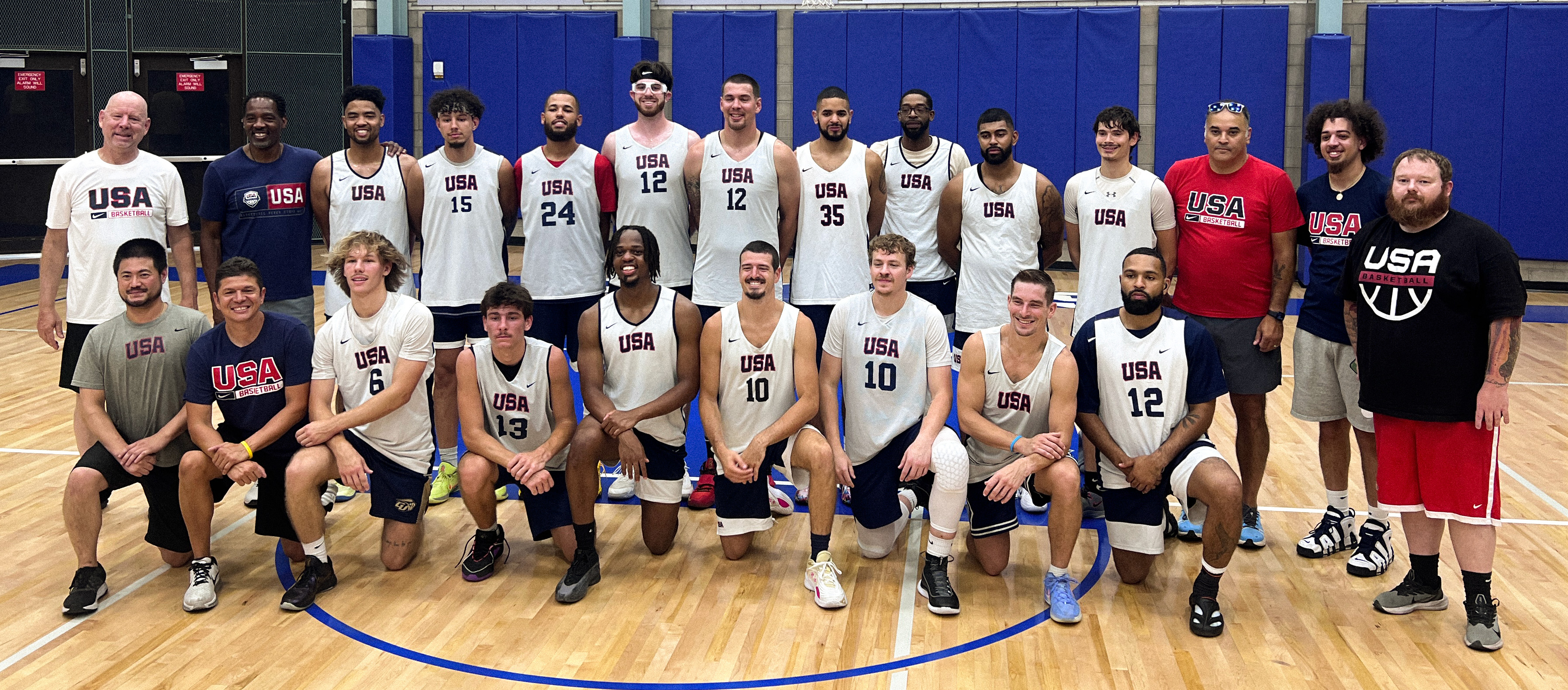 Team USA Deaf Men’s Basketball players and coaches pose together on an indoor court, smiling and wearing USA uniforms during training camp.