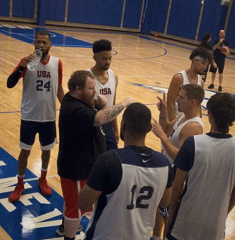 Team USA Deaf Men’s Basketball players gather in a huddle on the court during practice as a coach gives instructions in sign language.