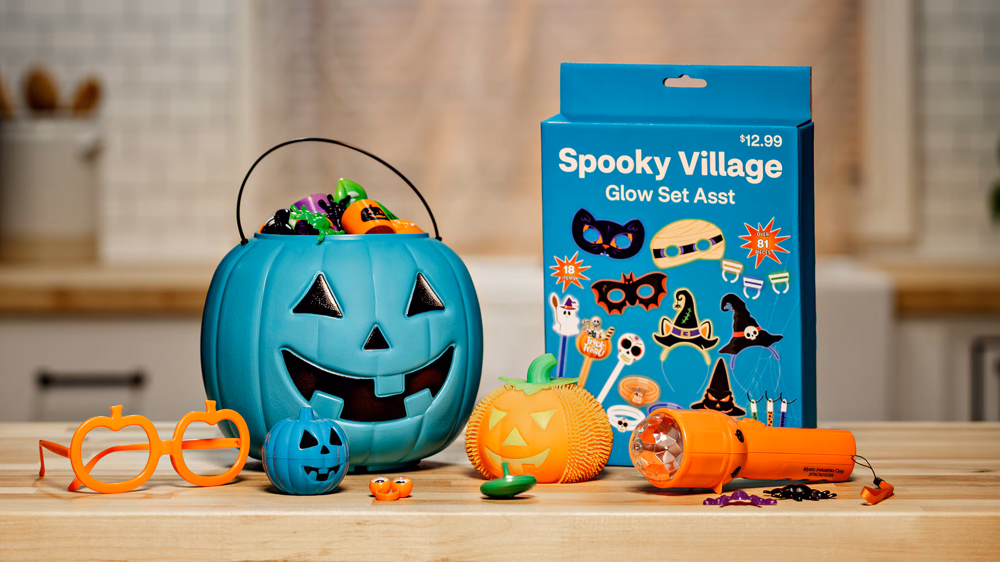 A teal pumpkin filled with small toys and trinkets sits beside a “Spooky Village Glow Set” box, representing allergy-safe, non-food treat options.