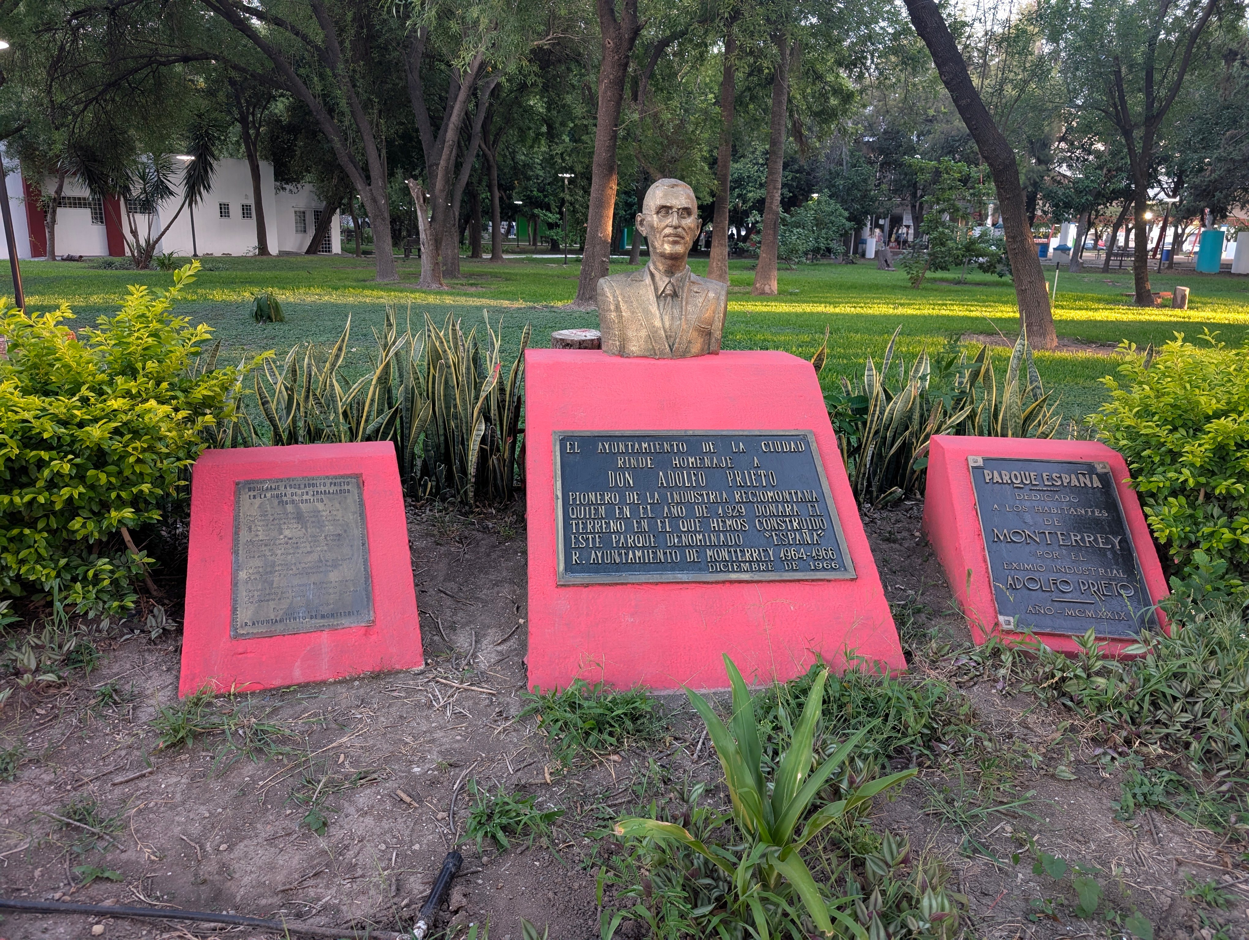 Busto de Adolfo Prieto y placas que identifican Parque España en Monterrey, rodeados de jardines.
