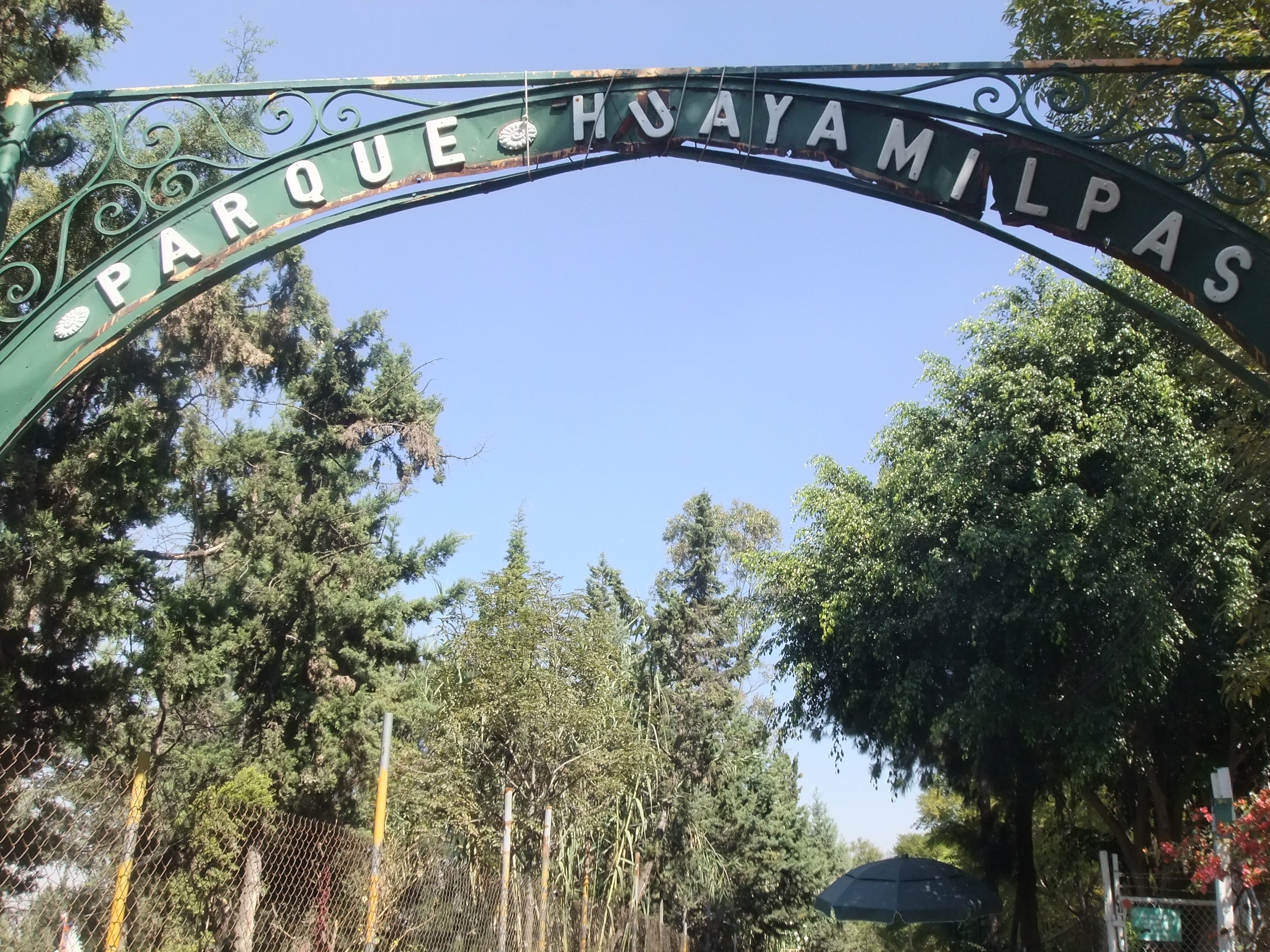 Arco de entrada con el nombre Parque Huayamilpas y arbolado, en Coyoacán.