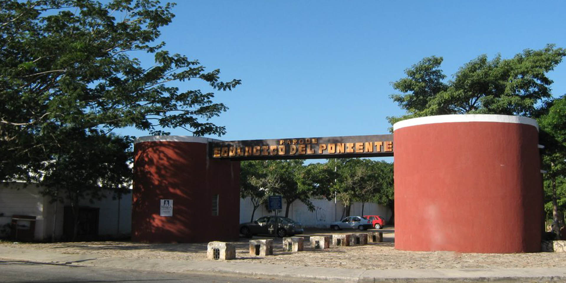 Entrada del Parque Ecológico del Poniente en Mérida, con letrero del parque entre pilares rojos.