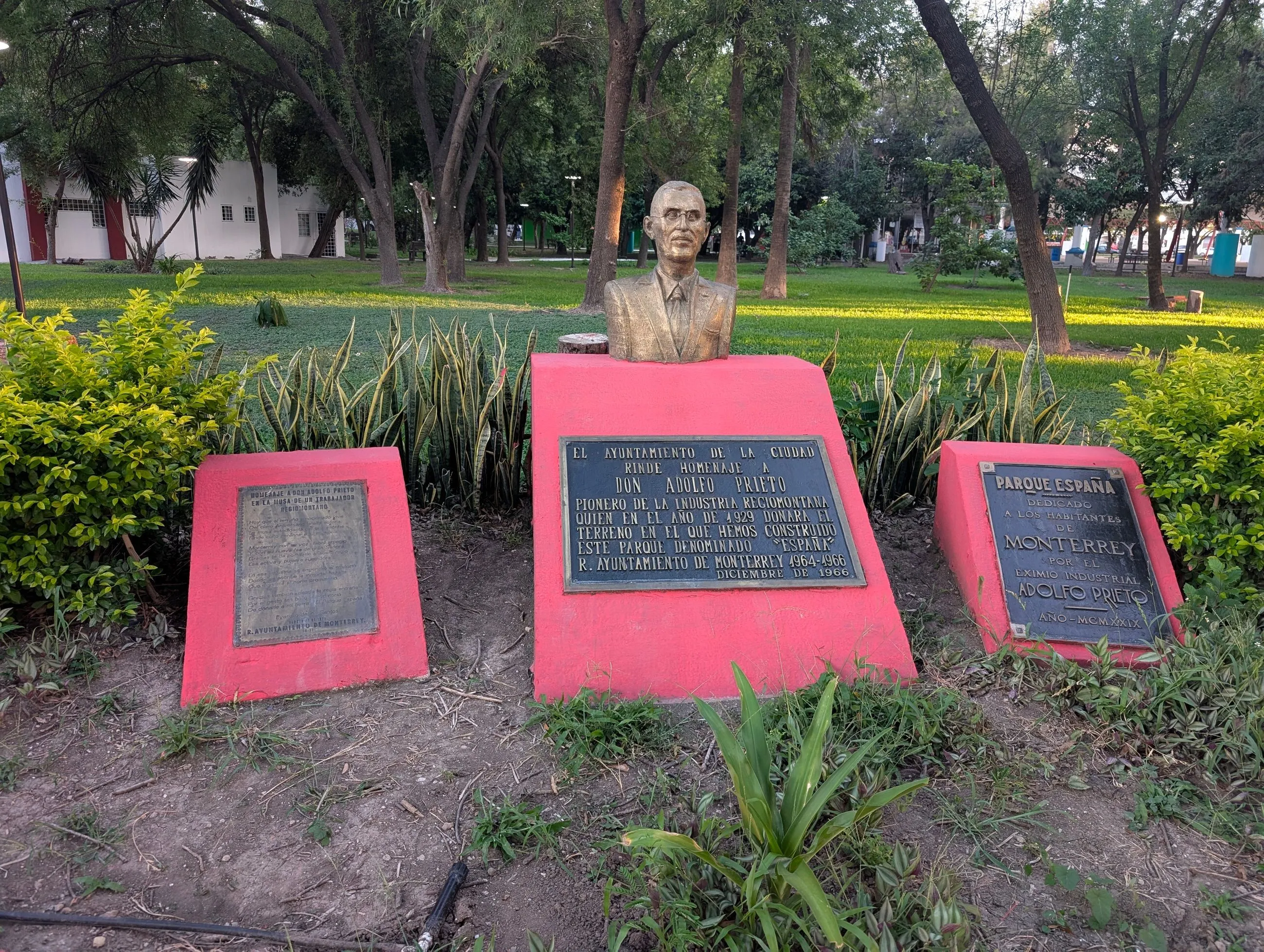 Busto de Adolfo Prieto y placas que identifican Parque España en Monterrey, rodeados de jardines.