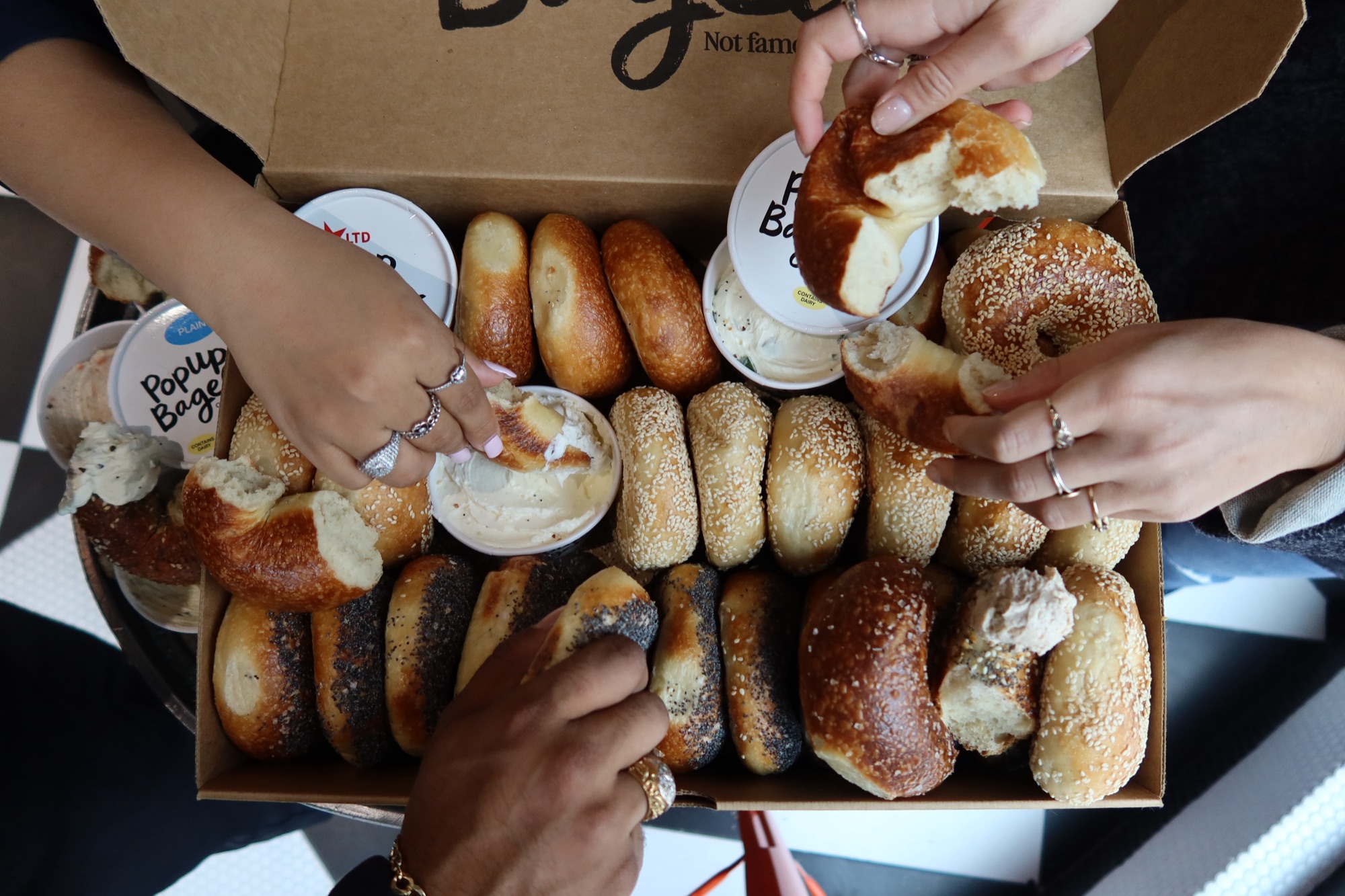 Hands sharing a box of PopUp Bagels, grip rip and dip