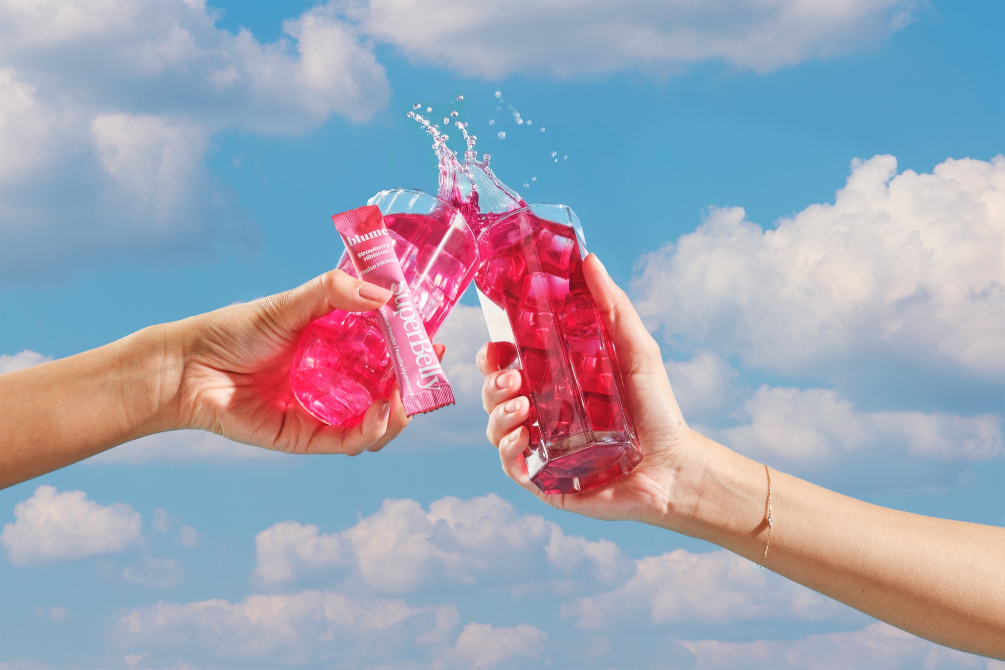 Two hands toasting glasses of Blume SuperBelly against a blue sky