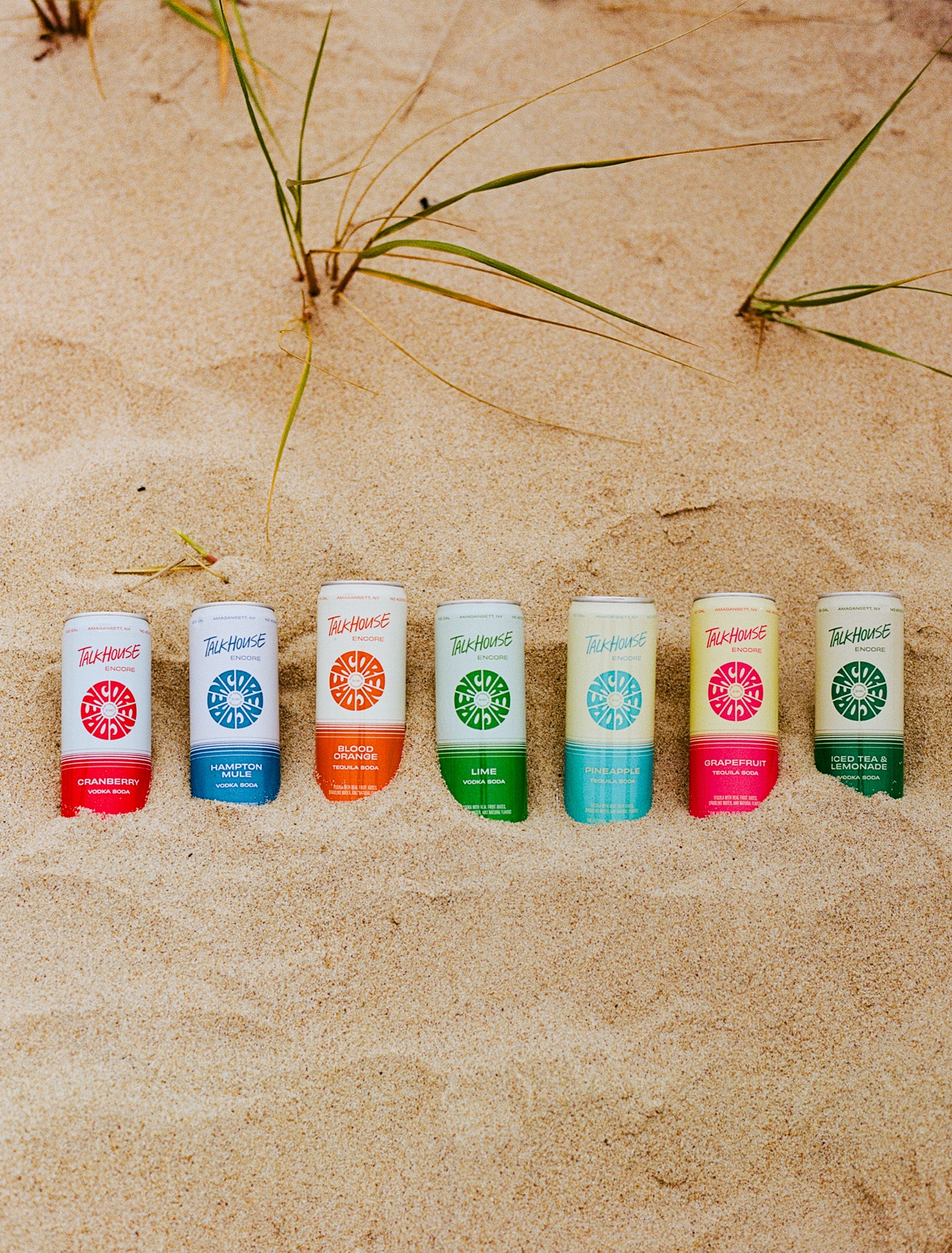 The seven Talkhouse Encore vodka and tequila seltzer flavors lined up in beach sand
