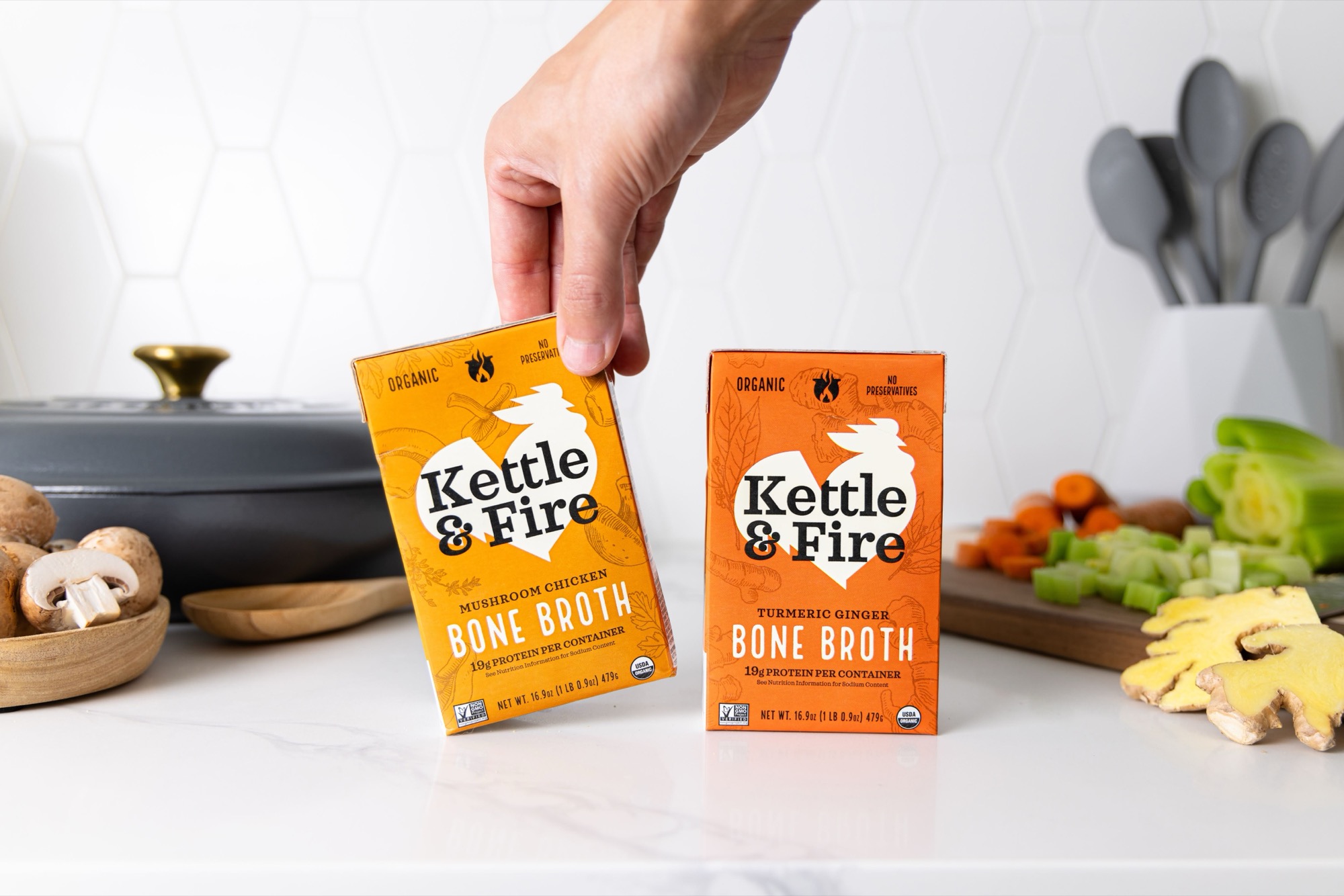 Two cartons of Kettle & Fire bone broth on a kitchen counter with fresh ingredients