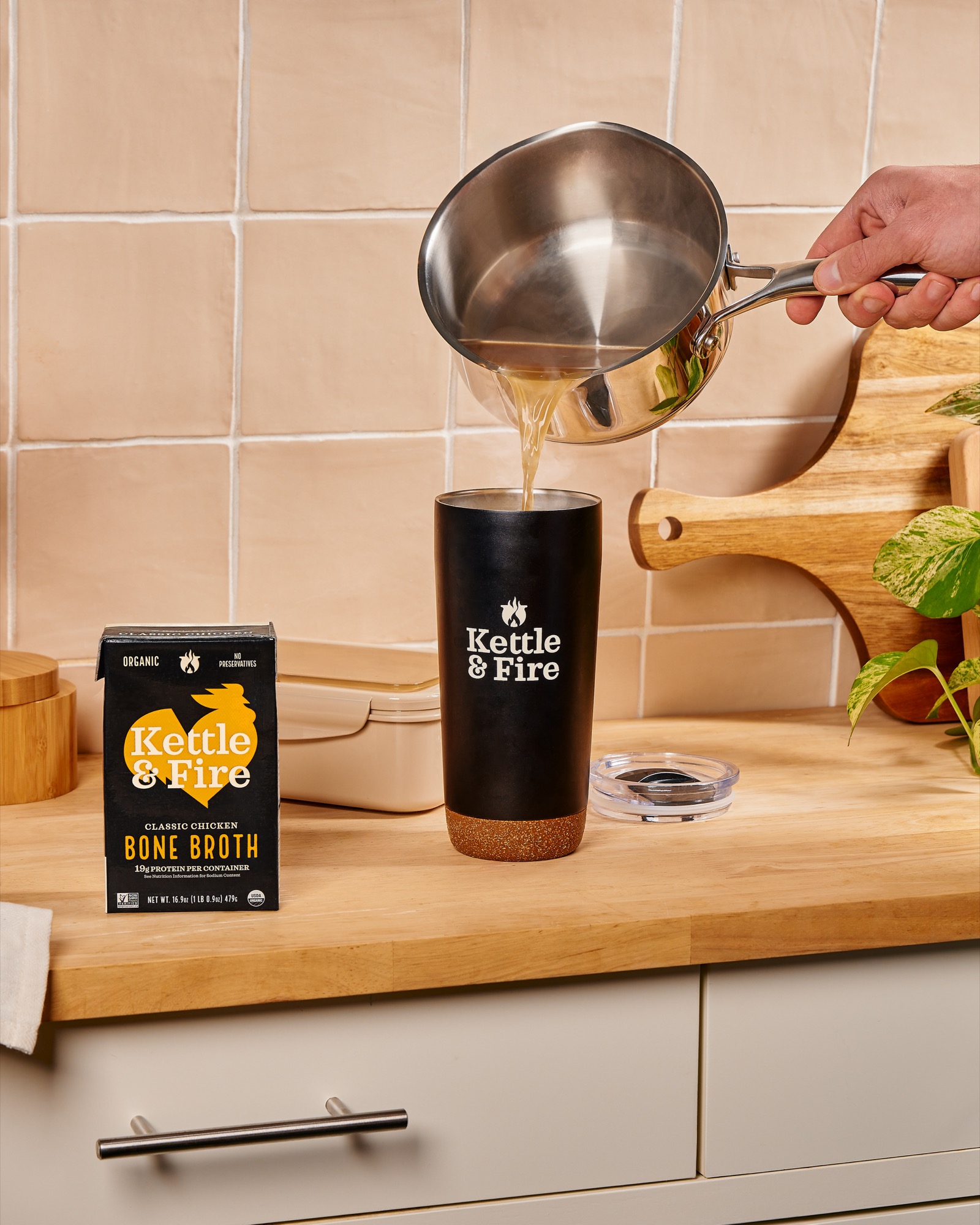 Bone broth being poured from a saucepan into a Kettle & Fire tumbler on a kitchen counter
