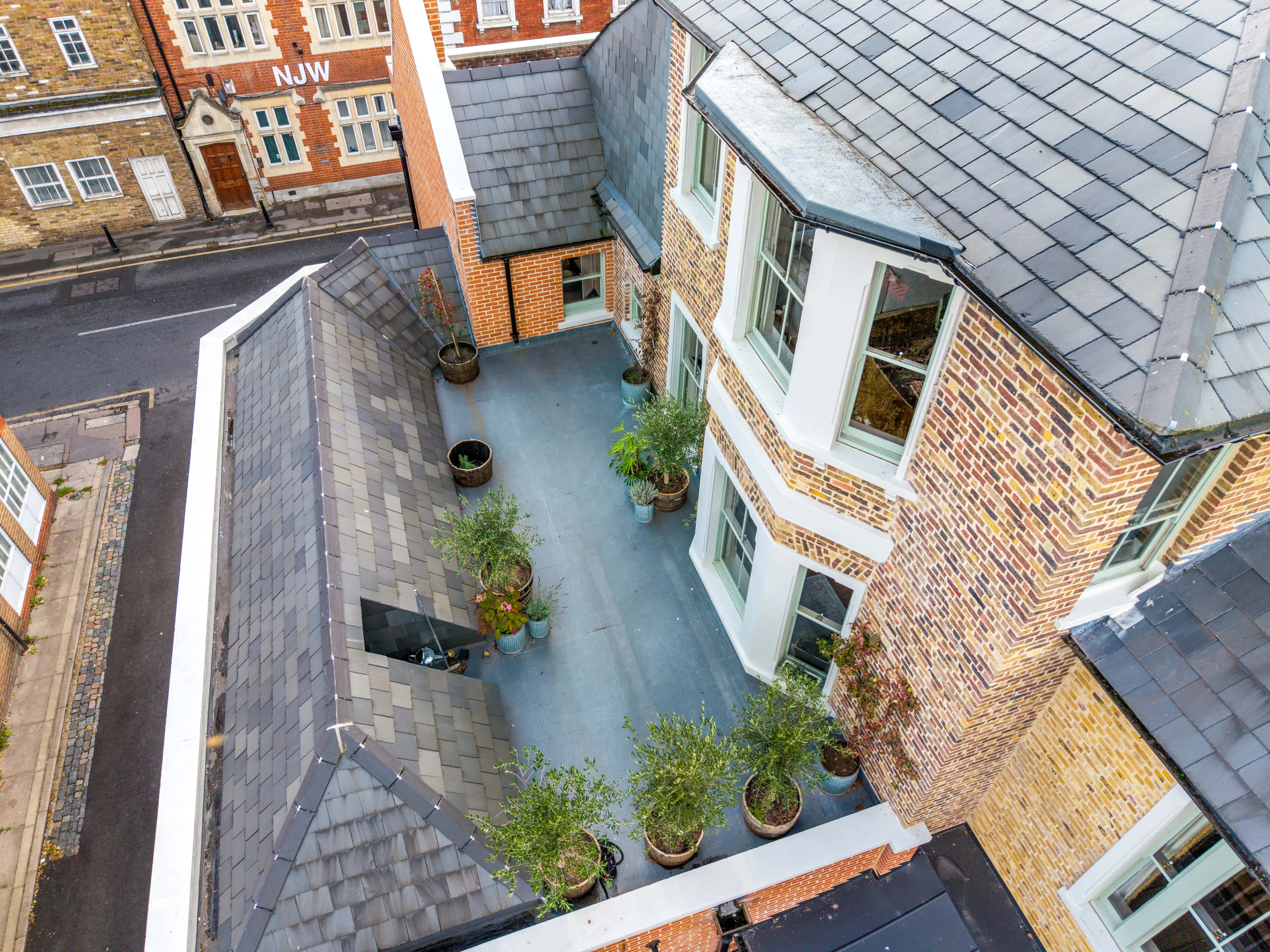 Aerial view of a brick building with potted plants on a flat rooftop terrace.
