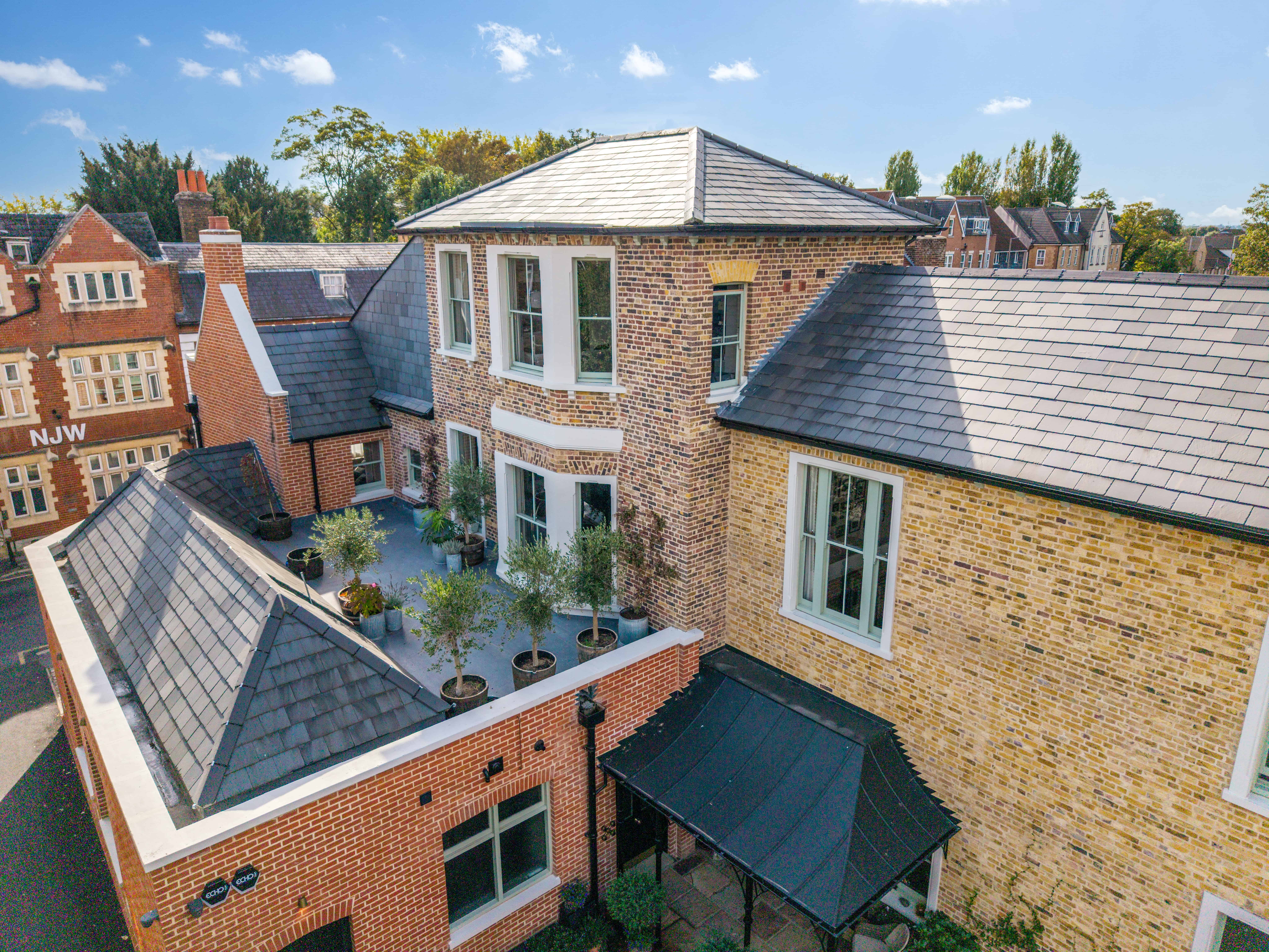 Aerial view of a multi-roof brick house with potted plants on a terrace under a clear blue sky.