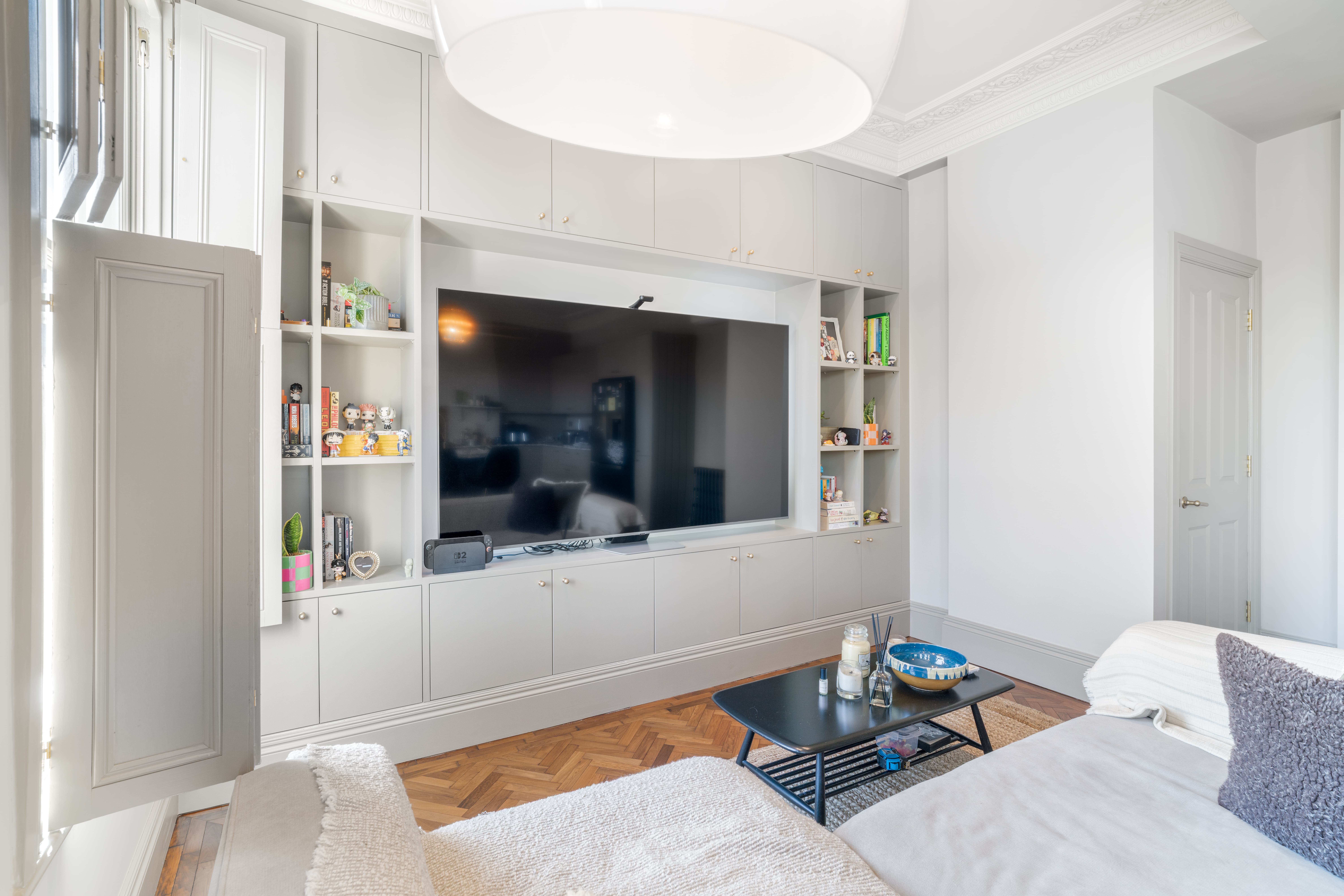 Modern living room with built-in gray cabinets, large TV, black coffee table, and light gray sofa.