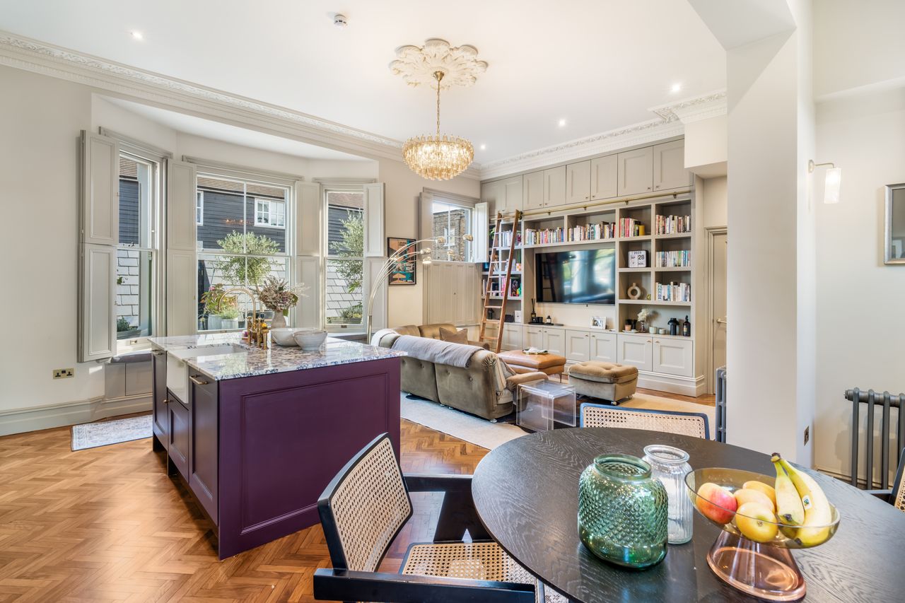 Bright living room with large bay windows, purple kitchen island, round dining table, and built-in bookshelves.