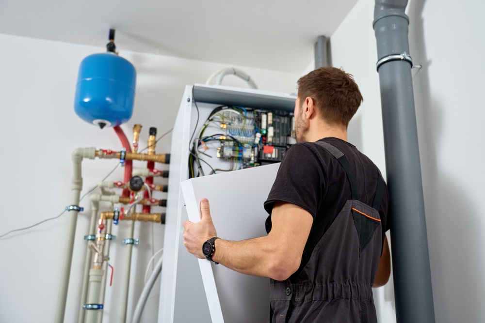 Technician in overalls inspecting the inner components of a boiler system in a utility room.