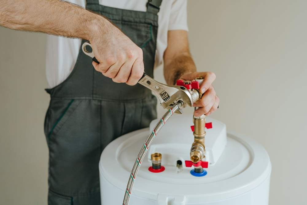 Person using a wrench to adjust a hose on a white water heater or boiler unit.